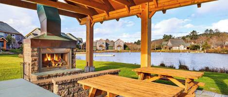 Ein Steinkamin mit Schornstein, eine Holzpergola und ein Picknicktisch in einem Garten mit Seeblick.