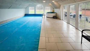 Una piscina interior amb sòl blau, grans finestres i una sauna.
