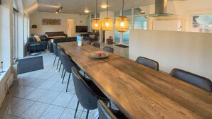 Una àmplia zona de dinar amb una taula de fusta llarga, cadires negres i llums penjants.