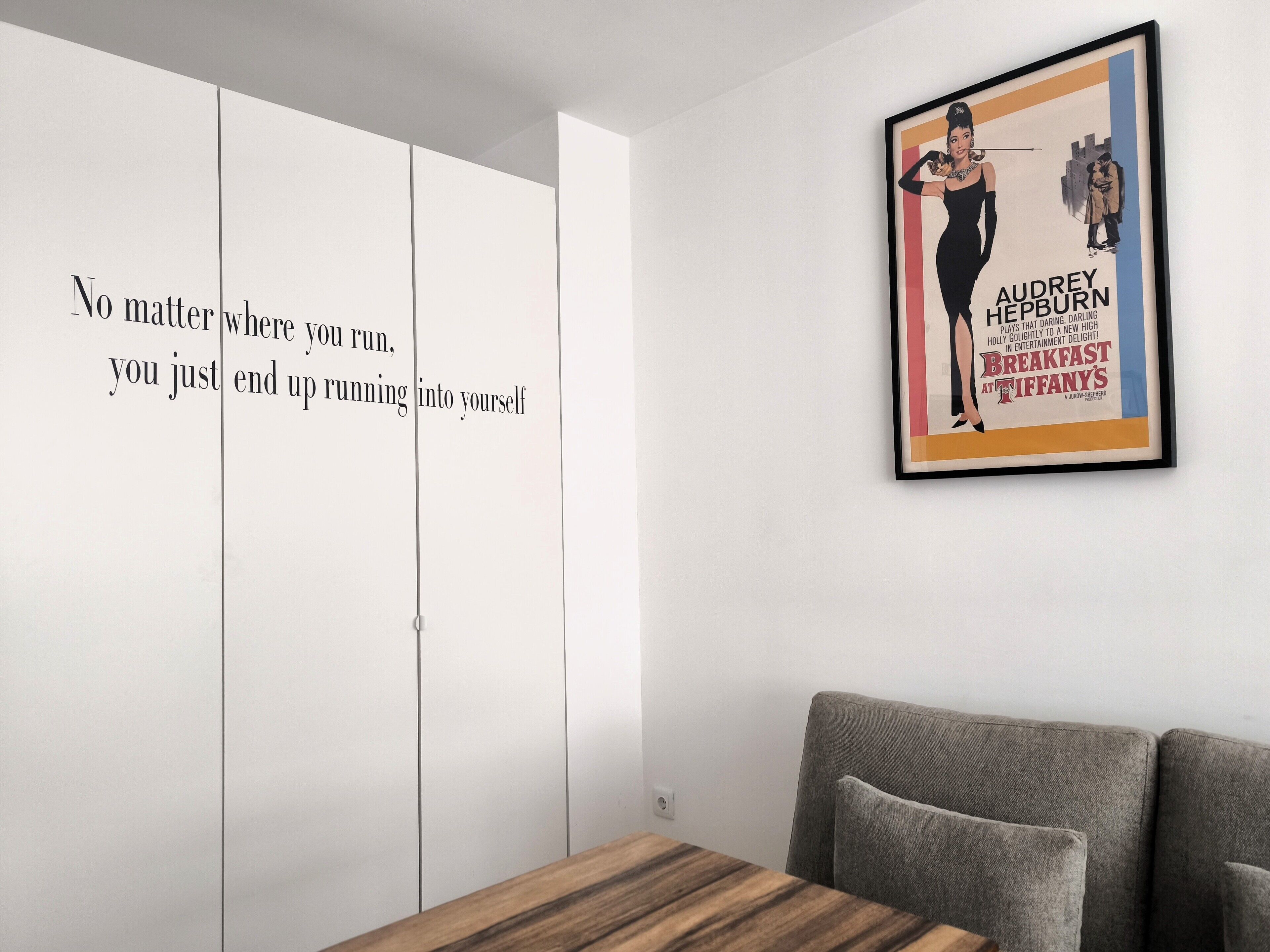 Una habitación con un cartel enmarcados de Audrey Hepburn en la pared, un armario blanco y un sofá gris.