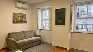 Una habitación con un sofá gris, un tapete verde y una ventana con vistas a edificios.