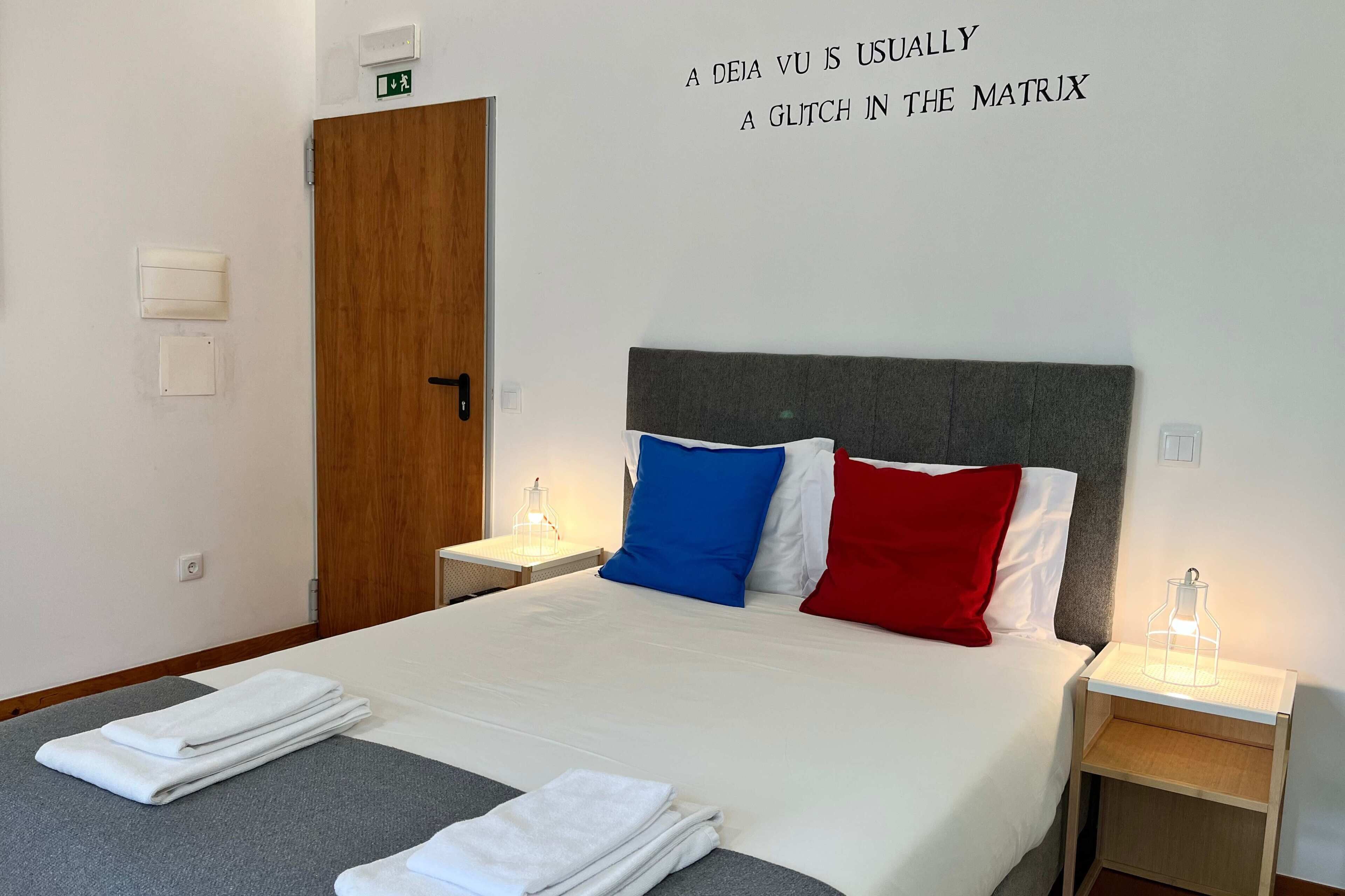 Habitación de hotel con cama, dos mesitas de noche y una pared con una cita de Matrix.