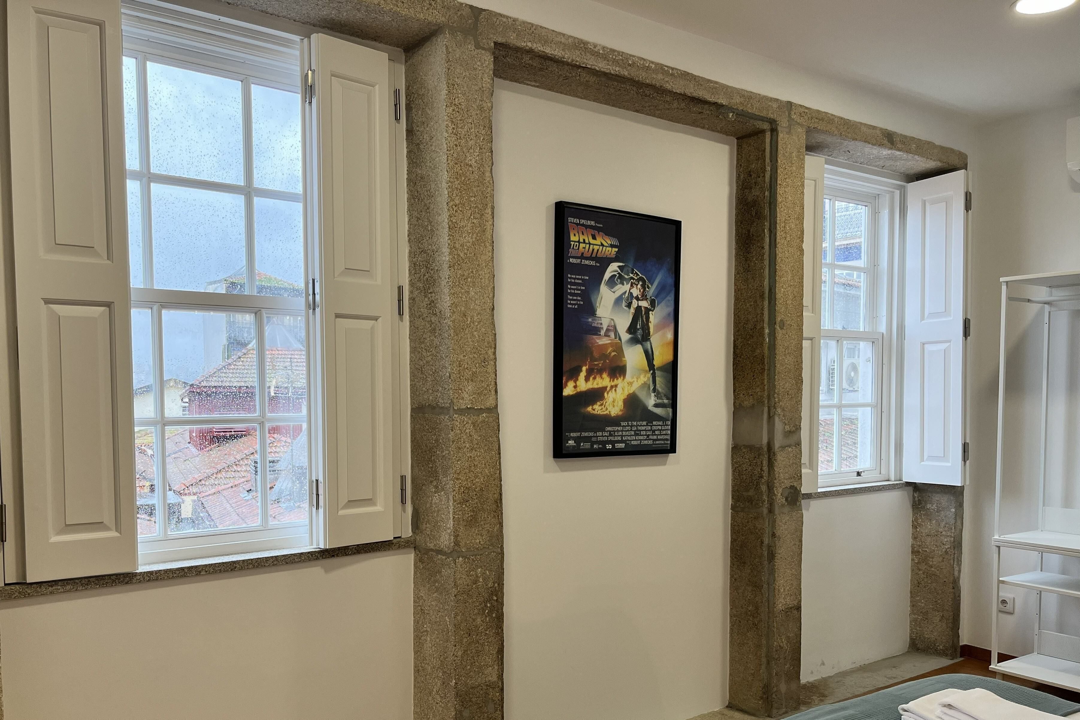 A room with a stone accent wall, a poster of 'Back to the Future', and a view of buildings outside through a window.