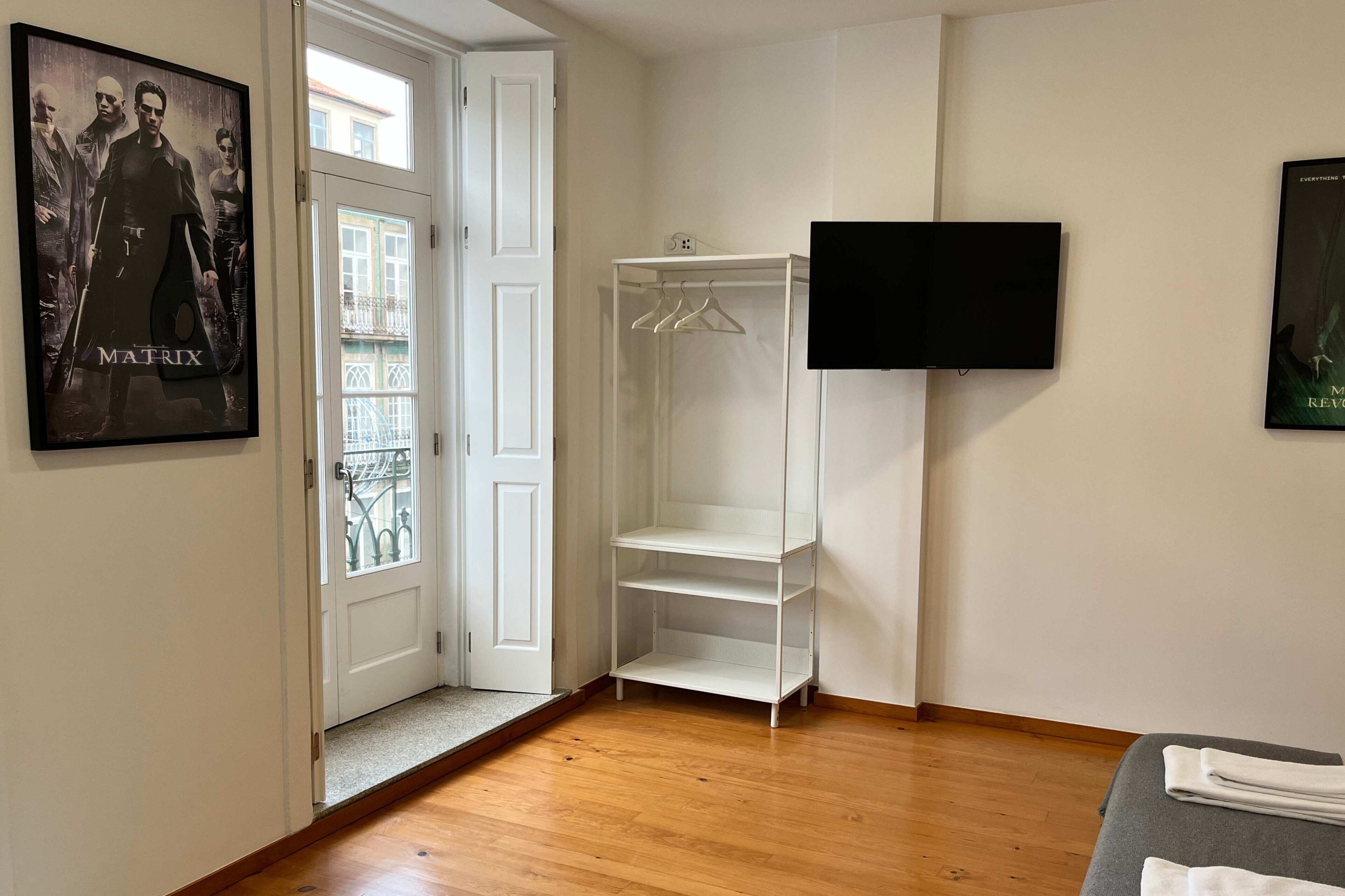 A room with a wooden floor, a white wardrobe, a TV mounted on the wall, and a poster of 'The Matrix' on the door.