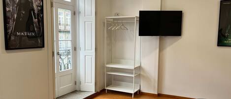 A room with a wooden floor, a white wardrobe, a TV mounted on the wall, and a poster of 'The Matrix' on the door.