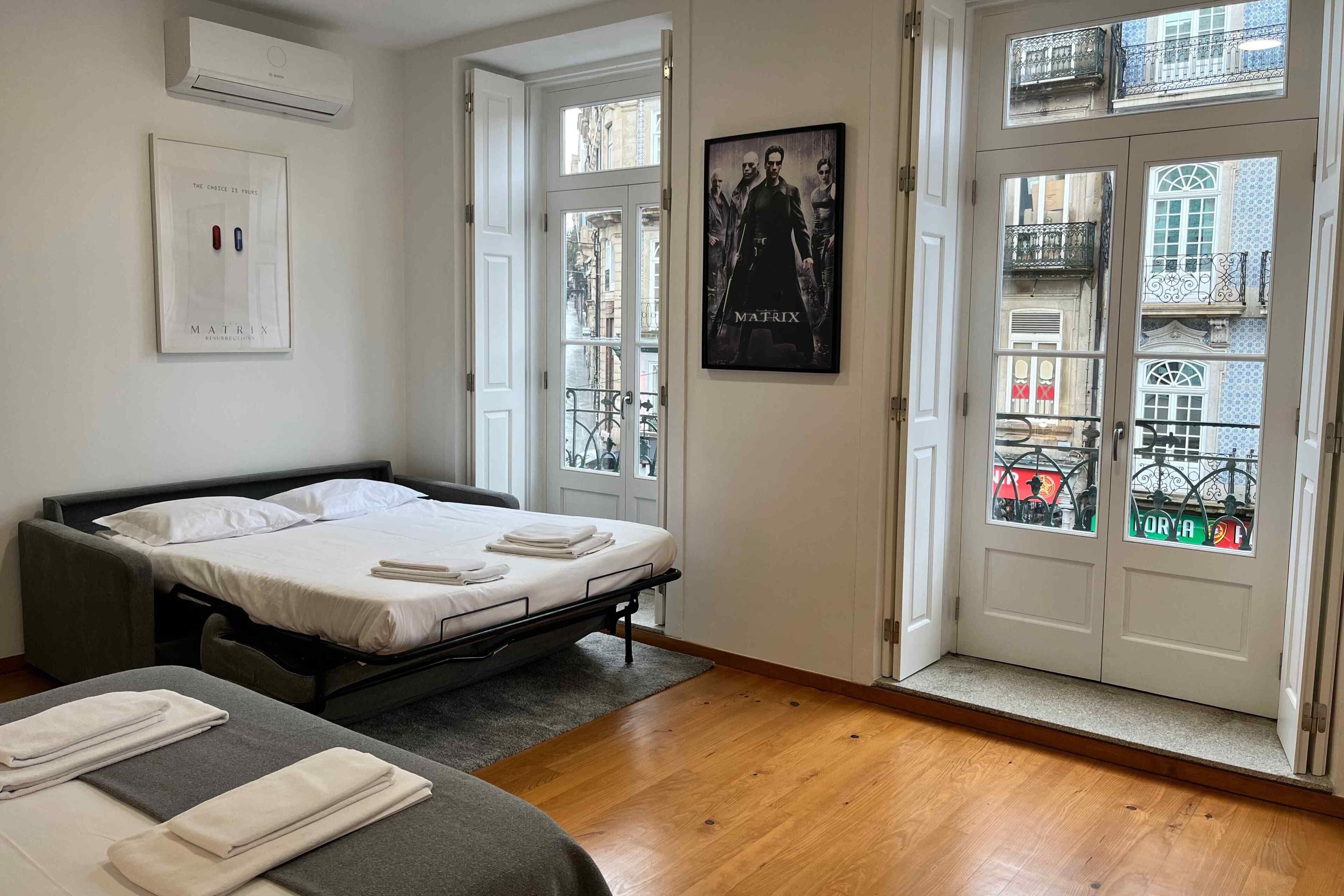 Habitación de hotel con cama, sofá, un cartel y una puerta que da a un balcón.