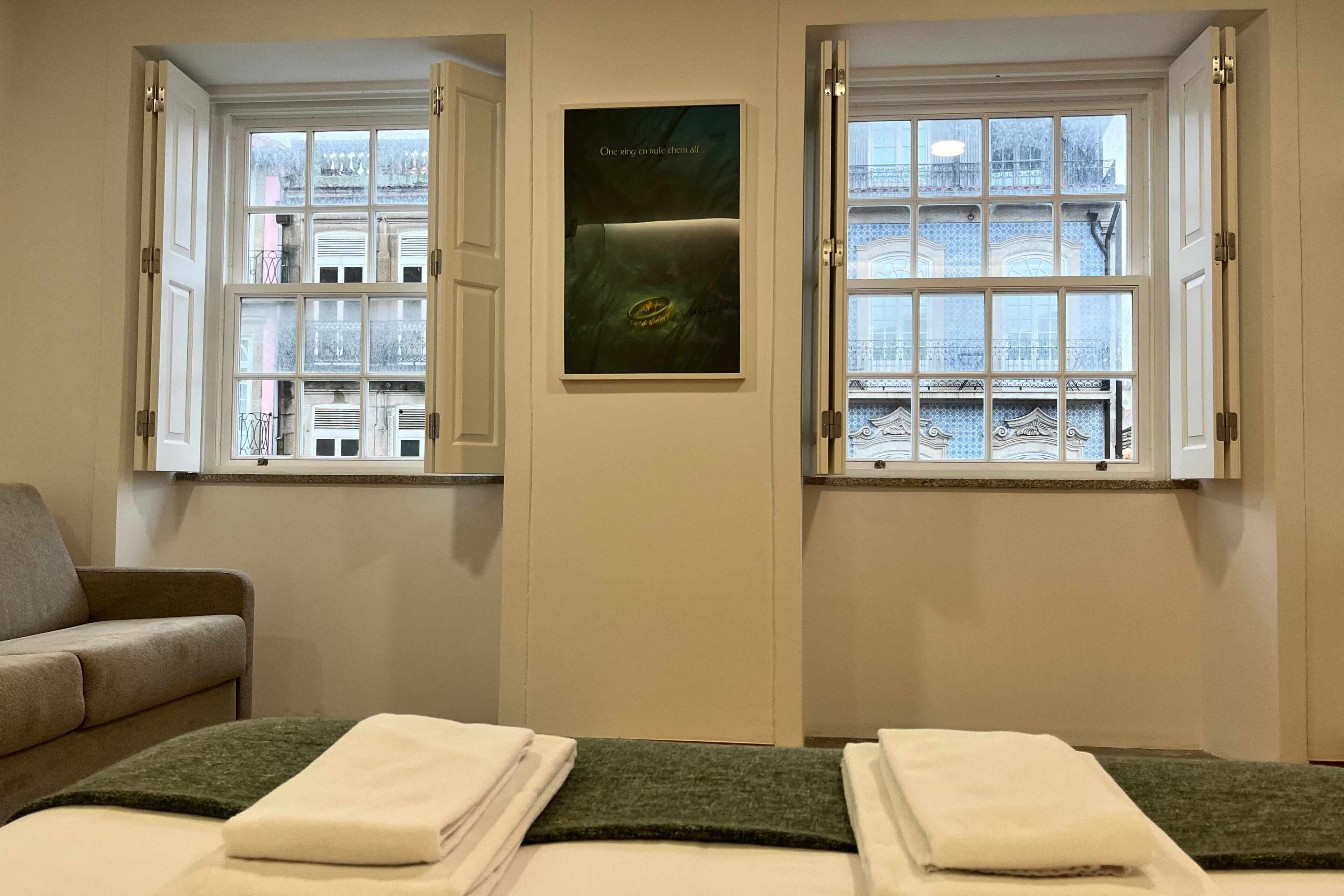 Habitación de hotel con dos camas, un sofá y grandes ventanas con vistas a edificios.
