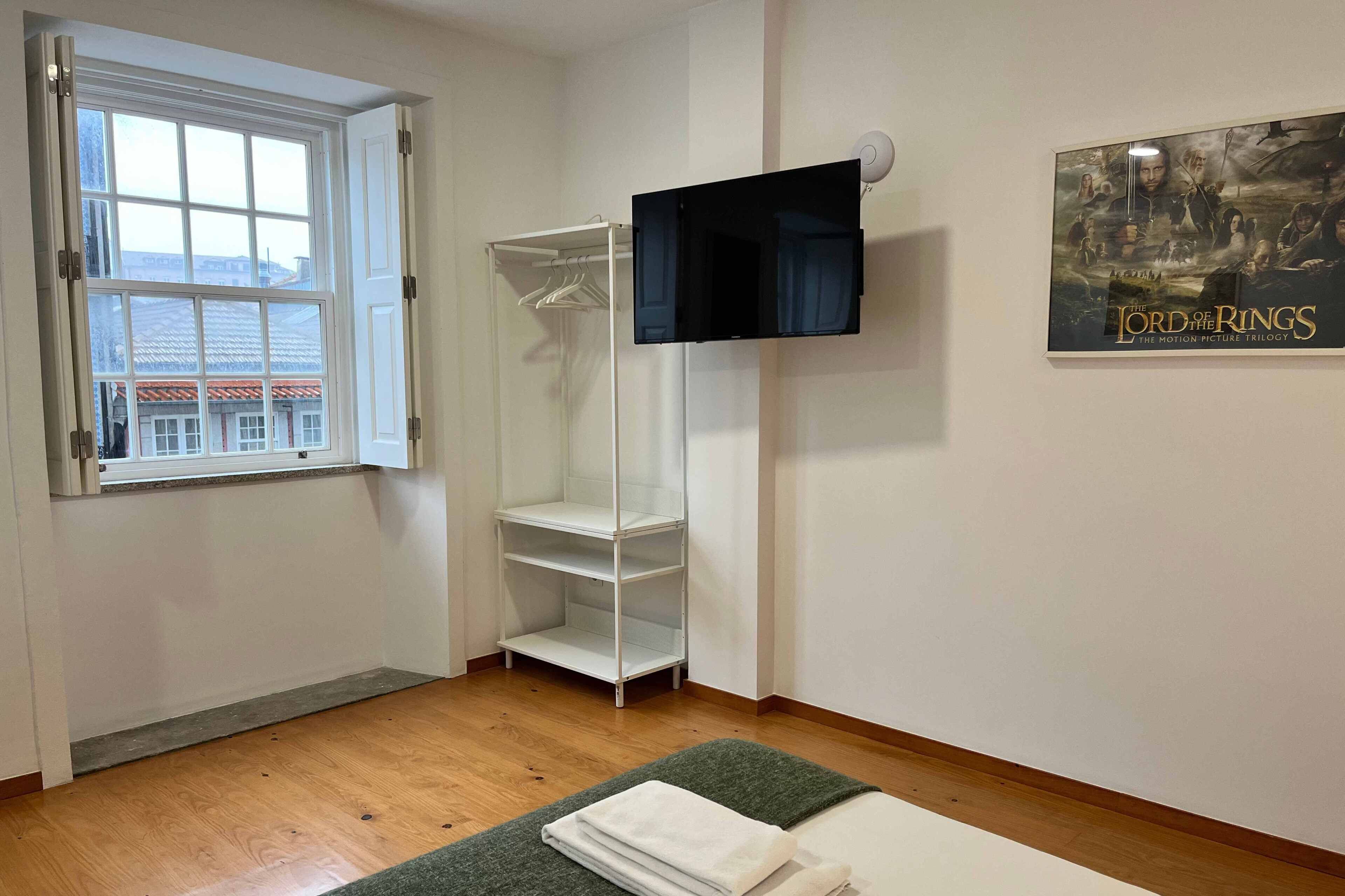 A room with a window, a white wardrobe, a flat-screen TV, and a poster of 'The Lord of the Rings' trilogy.