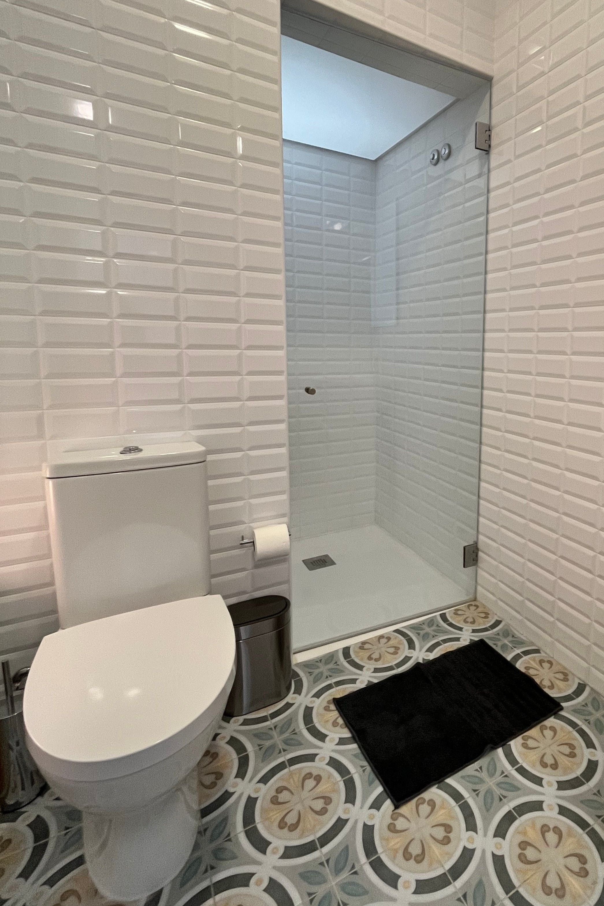 A bathroom with a toilet, a shower, and patterned floor tiles.