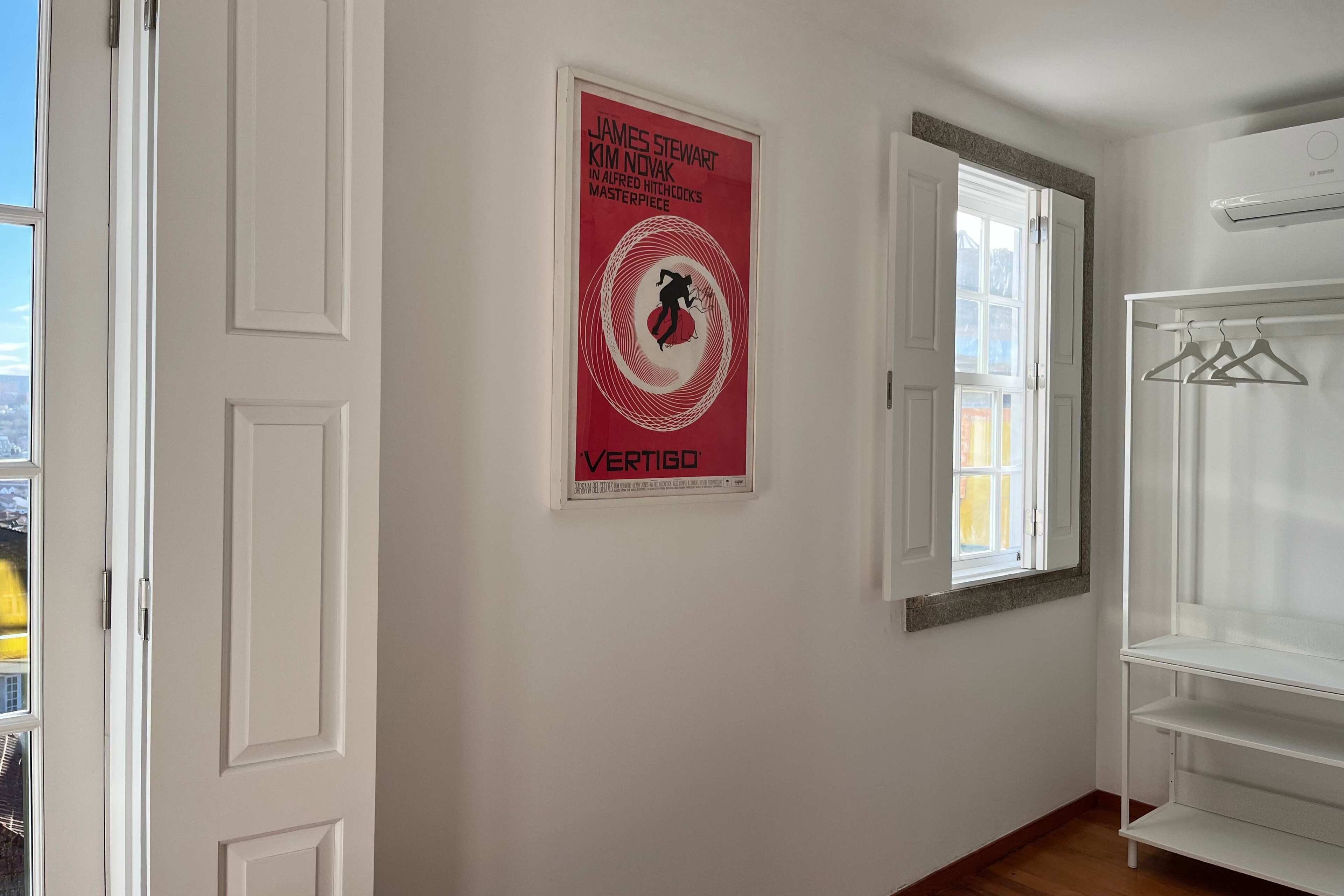 A room with a poster on the wall, a window, and a white wardrobe.