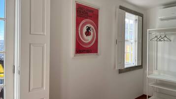 A room with a poster on the wall, a window, and a white wardrobe.