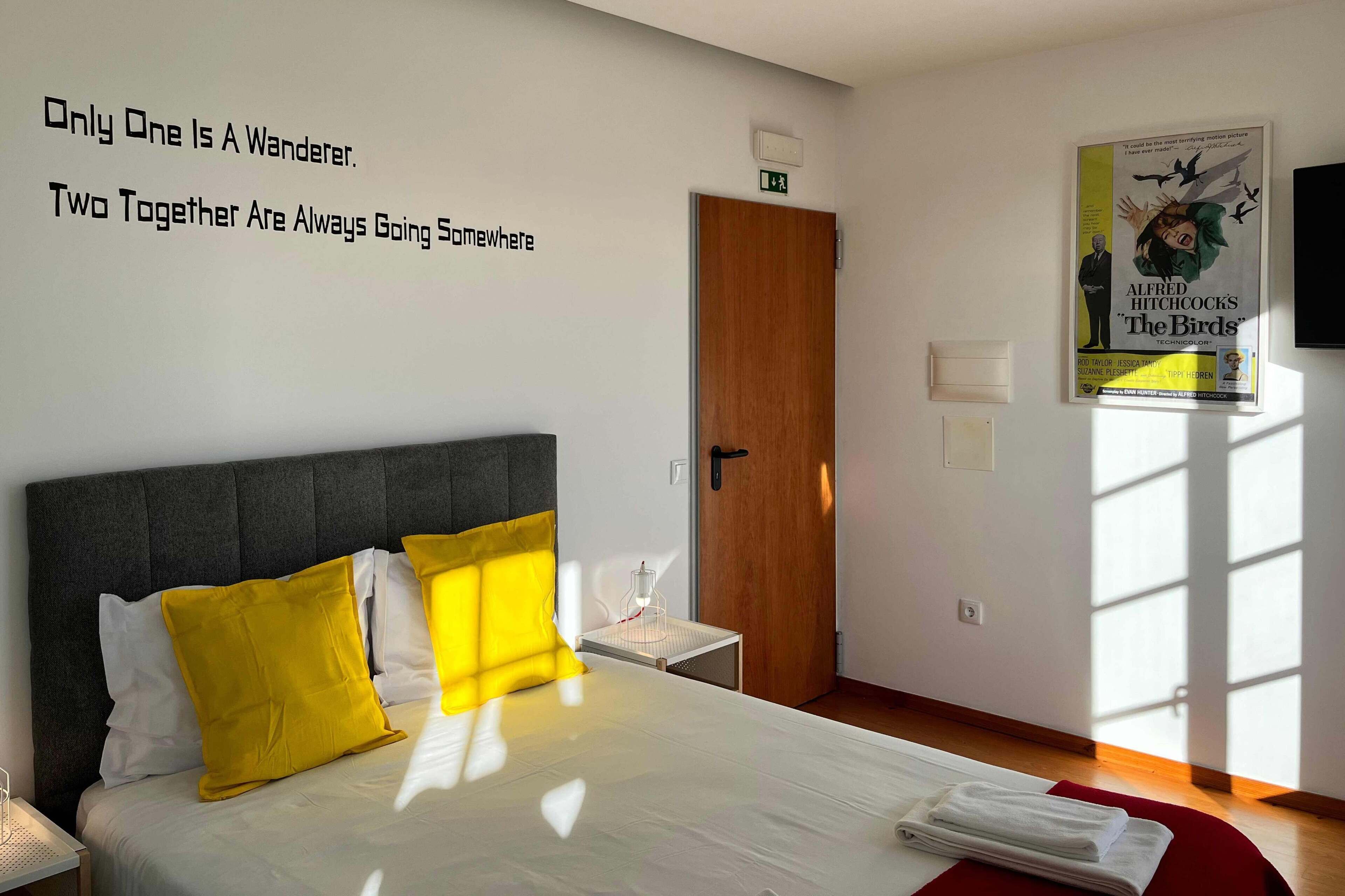 A hotel room with a bed, a bedside table, a wall with motivational quotes, a door, and a poster on the wall.