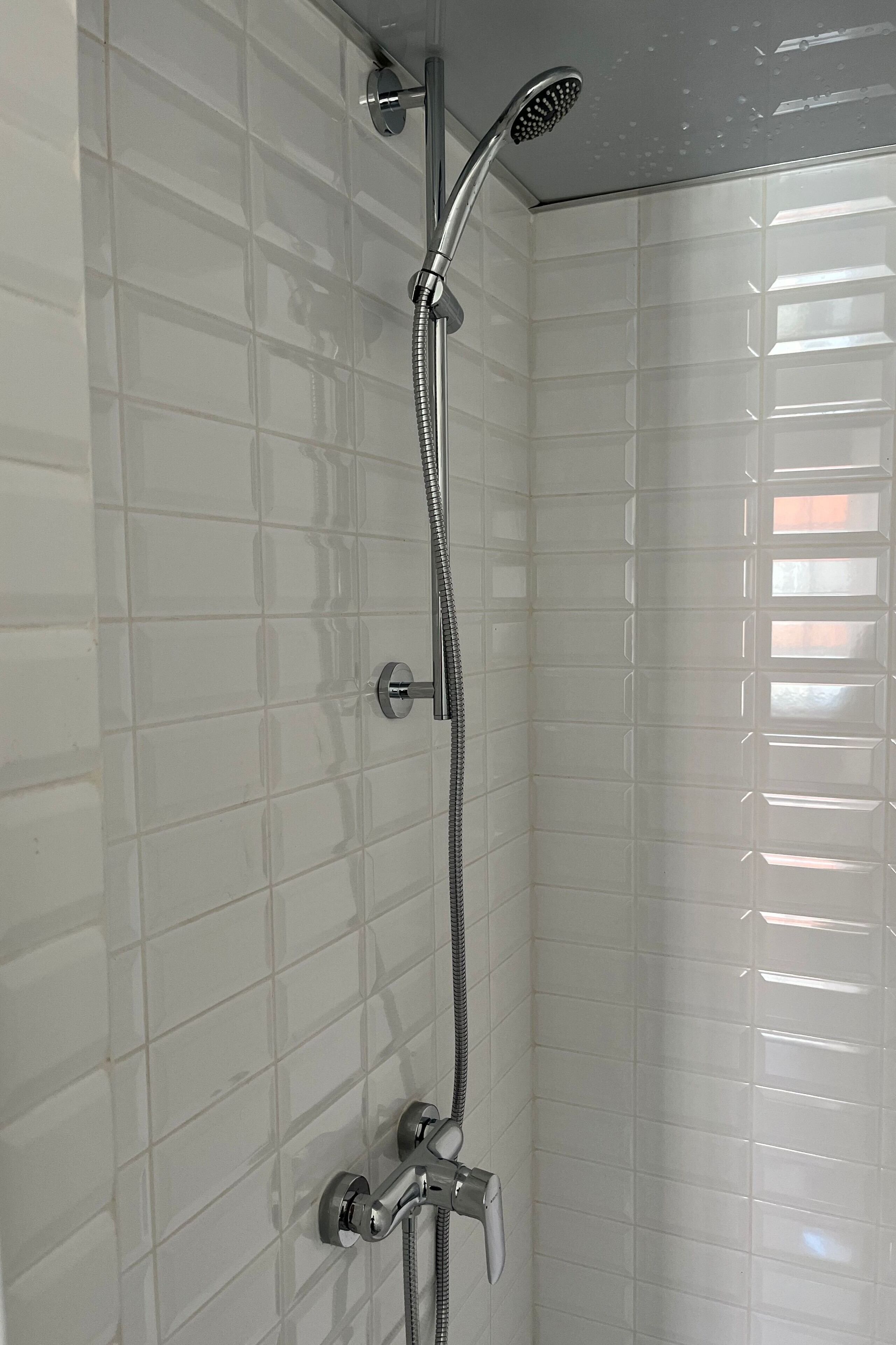 A shower with a handheld showerhead and a wall-mounted faucet.