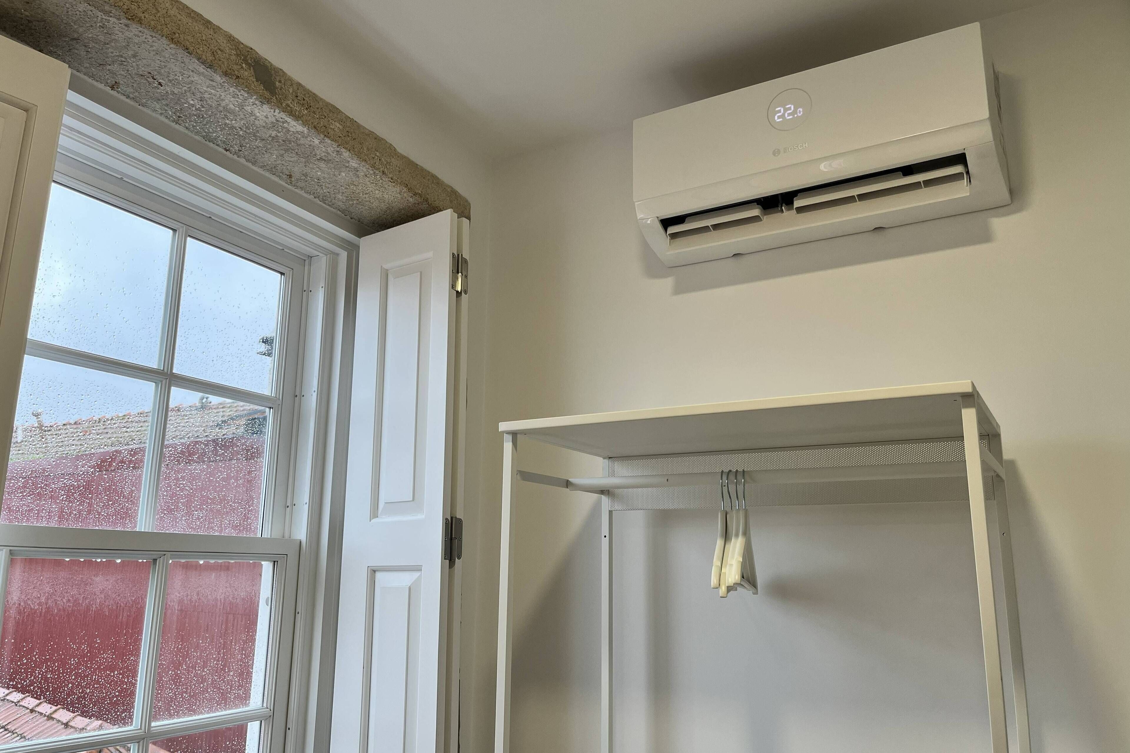 Een kamer met een witte airconditioning, een witte deur en een raam met uitzicht op een rood gebouw.