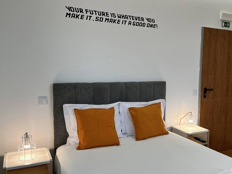 Una cama bien hecha con almohadas blancas y mostaza, un cabecero tapizado en gris y una cita motivacional en la pared.