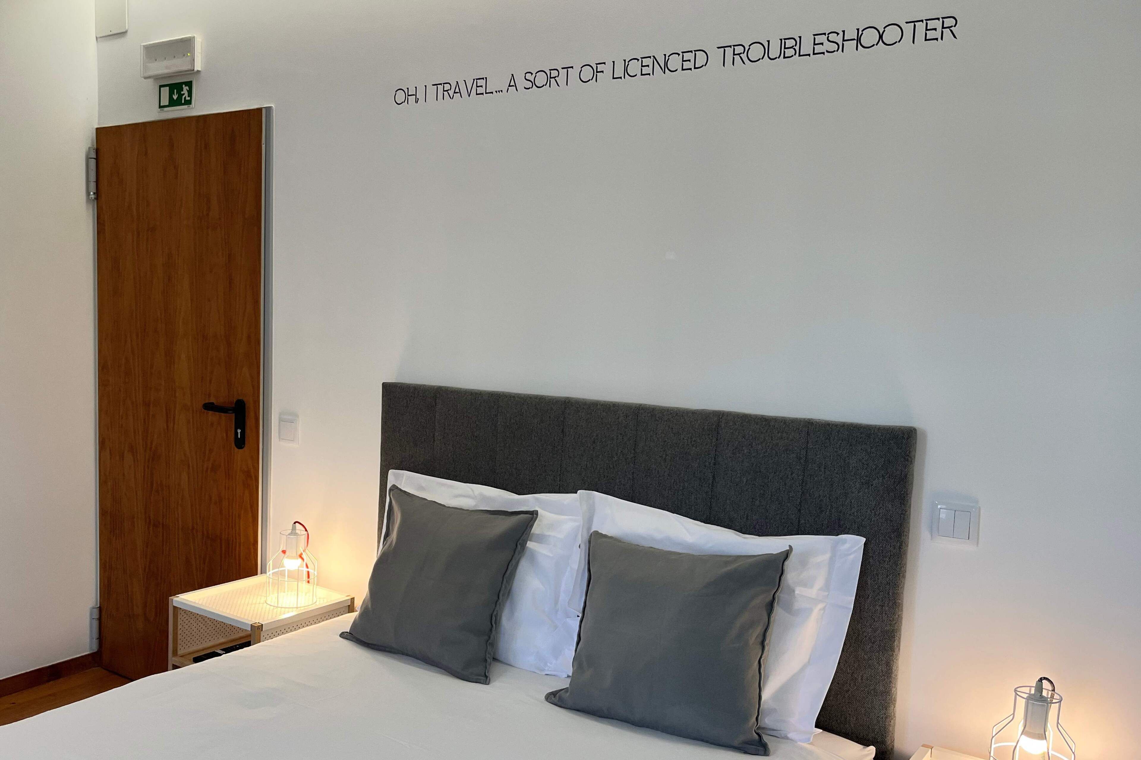A hotel room with a bed, two bedside lamps, a wooden door, and a wall sign.