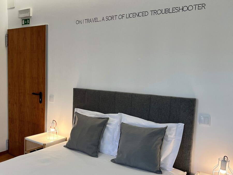 A hotel room with a bed, two bedside lamps, a wooden door, and a wall sign.