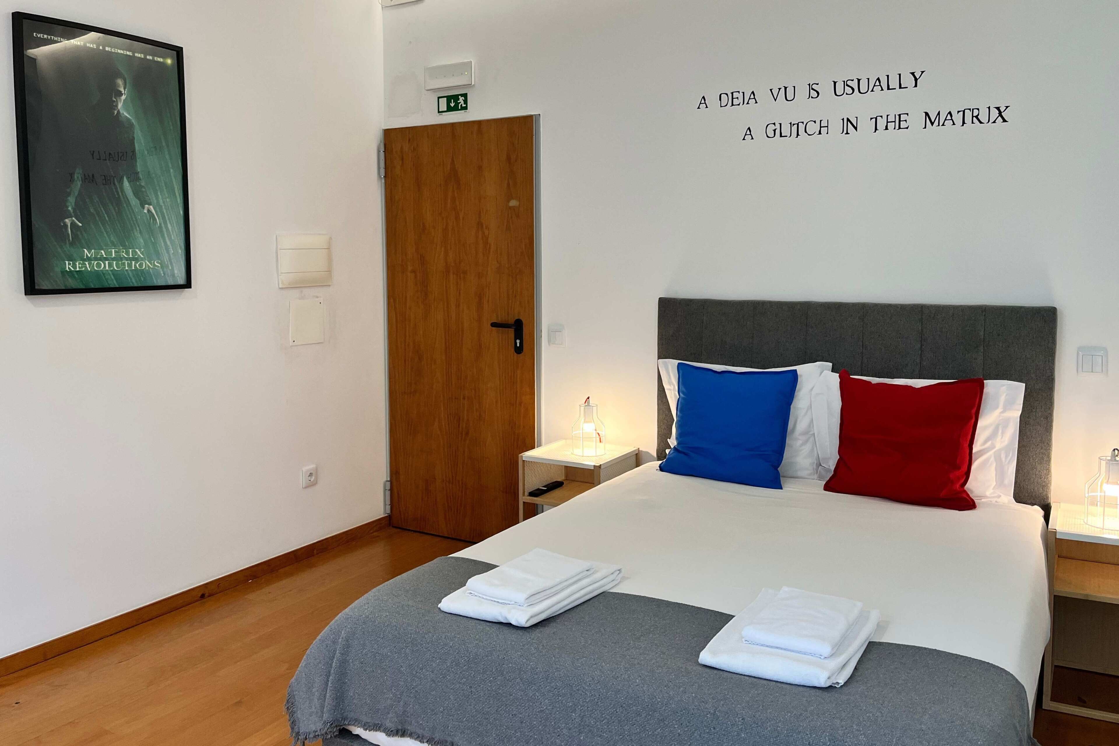 A hotel room with a bed, pillows, a nightstand, a wall poster, and a door.