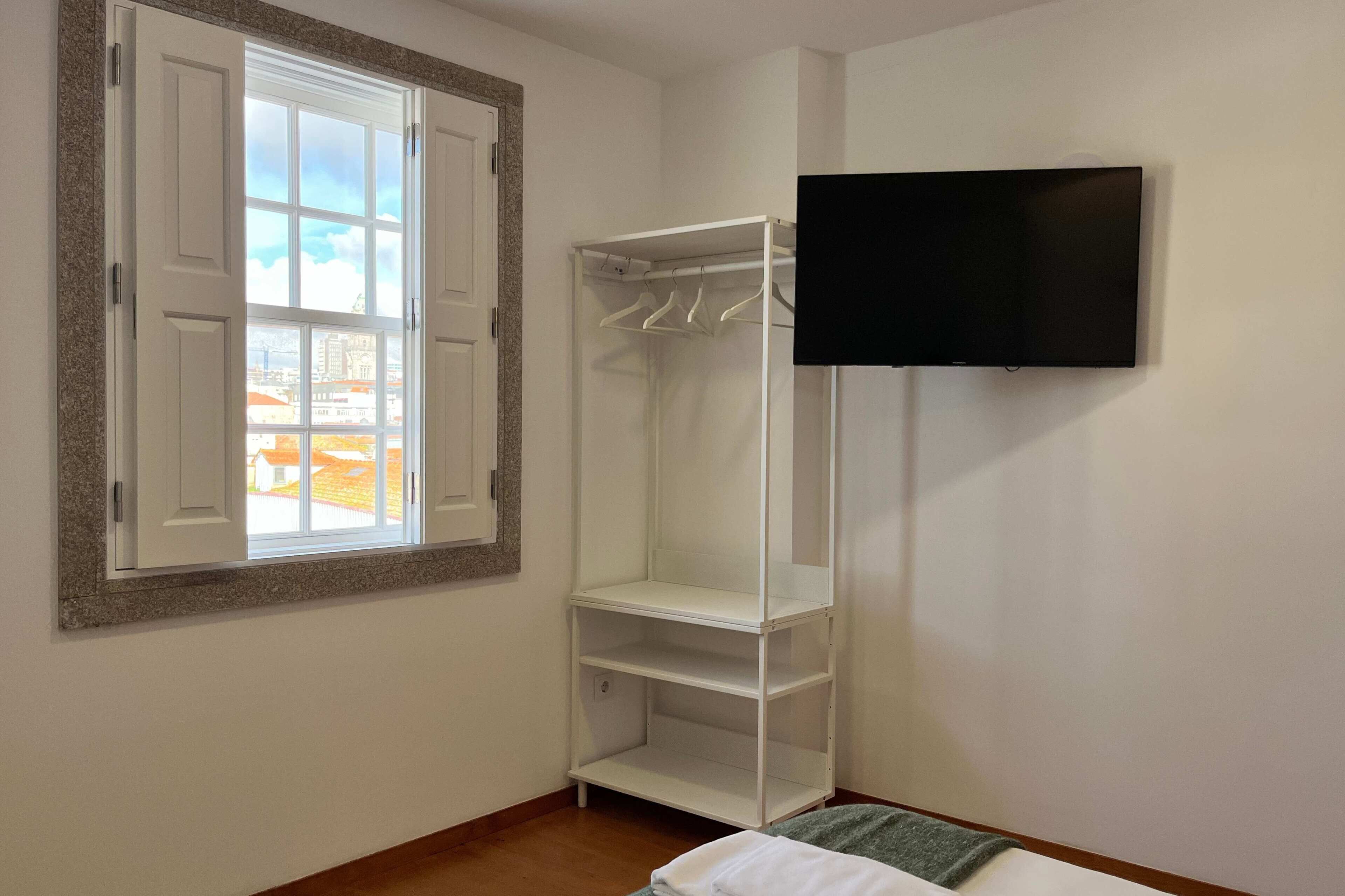 A room with a window, a white shelving unit, and a mounted television.