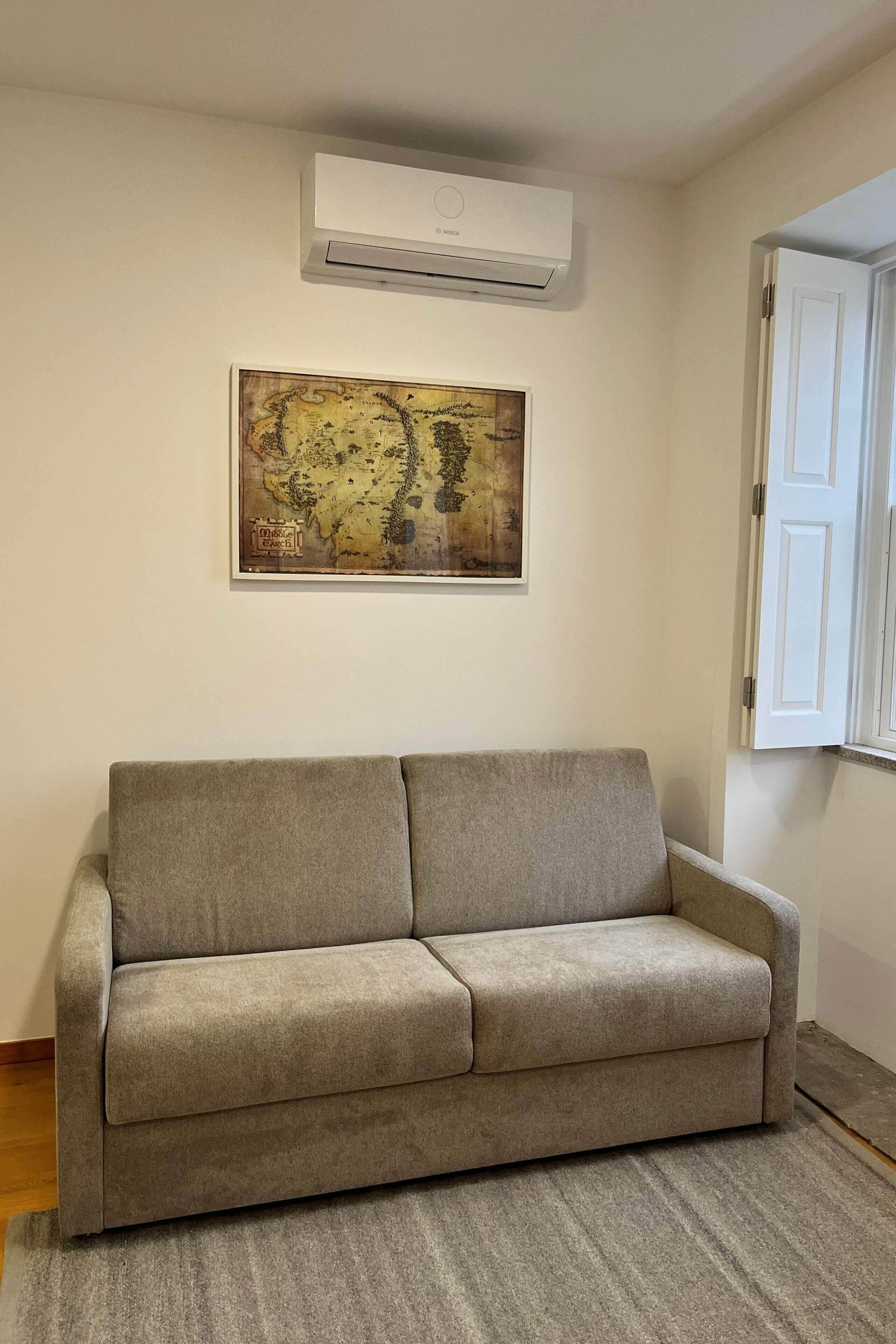 Un salon avec un canapé beige, un climatiseur fixé au mur et une carte encadrée accrochée au mur.