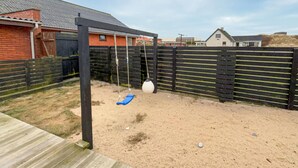 Ein sandiger Hinterhof mit Schaukel, Holzterrasse und schwarzem Zaun.