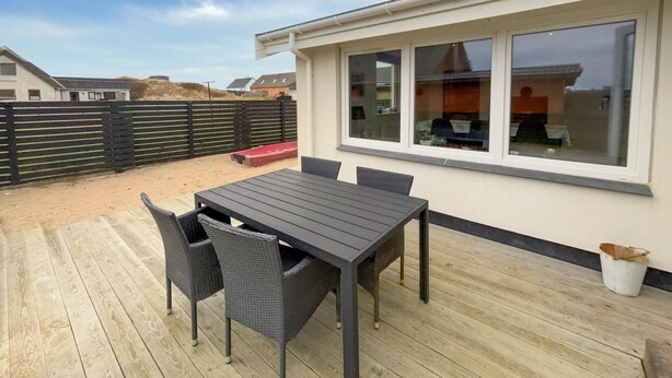Eine Terrasse im Freien mit Tisch und Stühlen, ein Holzdeck und ein Gebäude mit großen Fenstern.