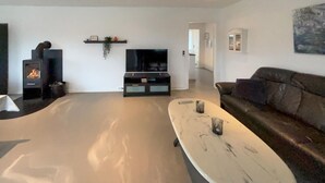 Ein modernes Wohnzimmer mit einem großen weißen Marmortisch, einer schwarzen Unterhaltungsanlage mit Flachbildfernseher, einem schwarzen Kamin und einem dunkelgrünen Ledersofa.
