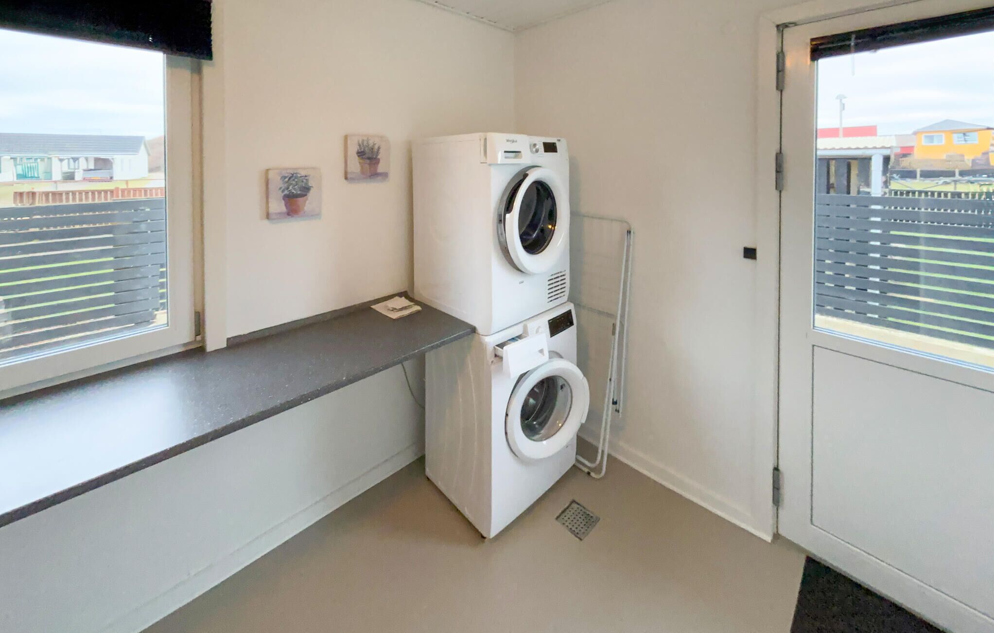 A laundry room with two stacked washing machines, a drying rack, and a window with blinds.