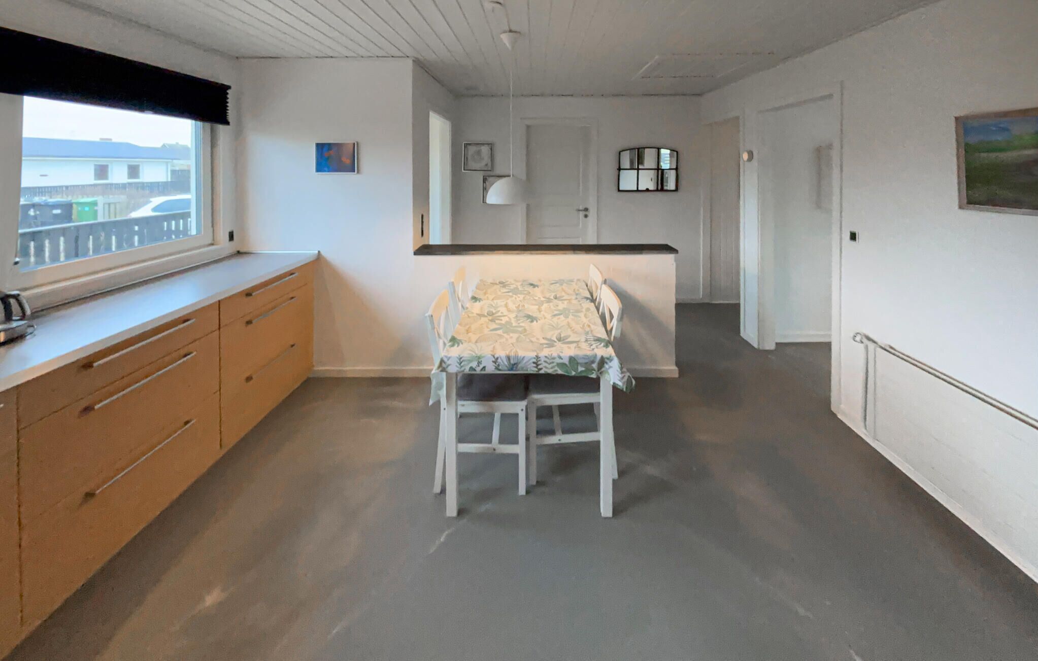 A room with a dining table and chairs, a window with a view, a kitchen area, and a door leading to another room.