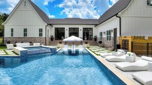 A swimming pool with lounge chairs and umbrellas, surrounded by a brick wall and white buildings. - Three Oaks Estate & Luxury Masters Tournament Retreat & Resort Pool (Harlem)