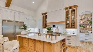 A modern kitchen with wooden cabinets, a central island, and a brick accent wall. - Three Oaks Estate & Luxury Masters Tournament Retreat & Resort Pool (Harlem)