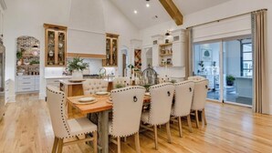 A spacious kitchen with wooden flooring, white cabinetry, and a dining area with a wooden table and upholstered chairs. - Three Oaks Estate & Luxury Masters Tournament Retreat & Resort Pool (Harlem)