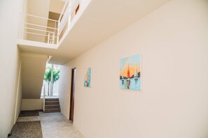 A hallway with a staircase leading to a balcony, a painting on the wall, and a door at the end. - Private Ocean View Retreat with Pool | Luxury HOM (Troncones)