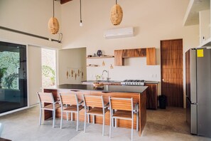 A modern kitchen with a central island, wooden chairs, and a built-in stove. - Private Ocean View Retreat with Pool | Luxury HOM (Troncones)