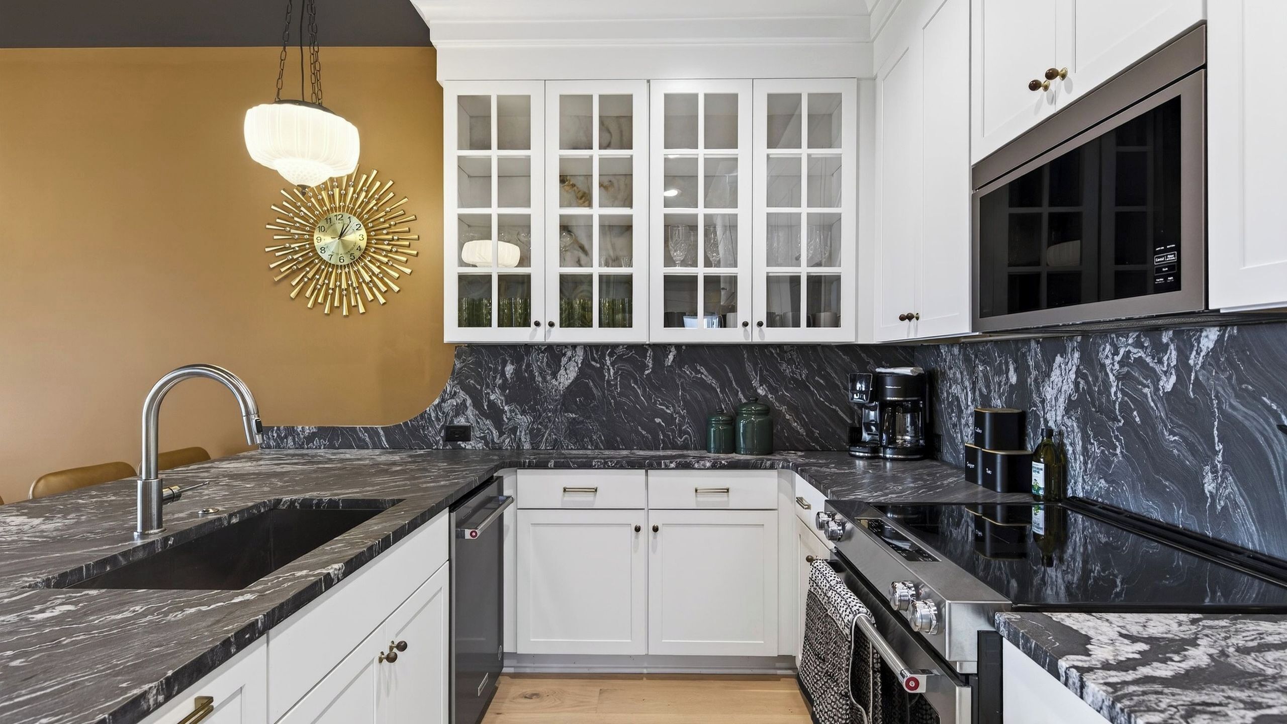 A modern kitchen with white cabinets, a black marble countertop, and a built-in oven.