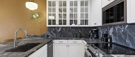 A modern kitchen with white cabinets, a black marble countertop, and a built-in oven.
