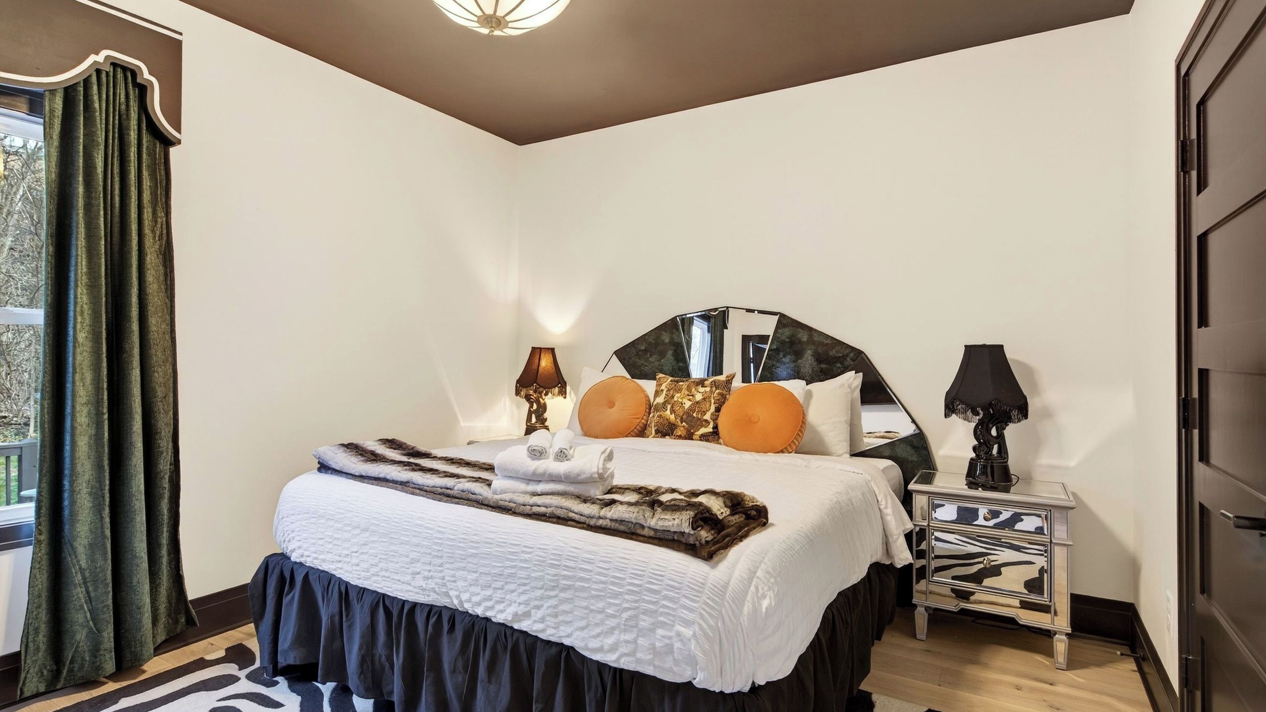 A bedroom with a bed, bedside tables, a mirror, and a view of the outdoors.