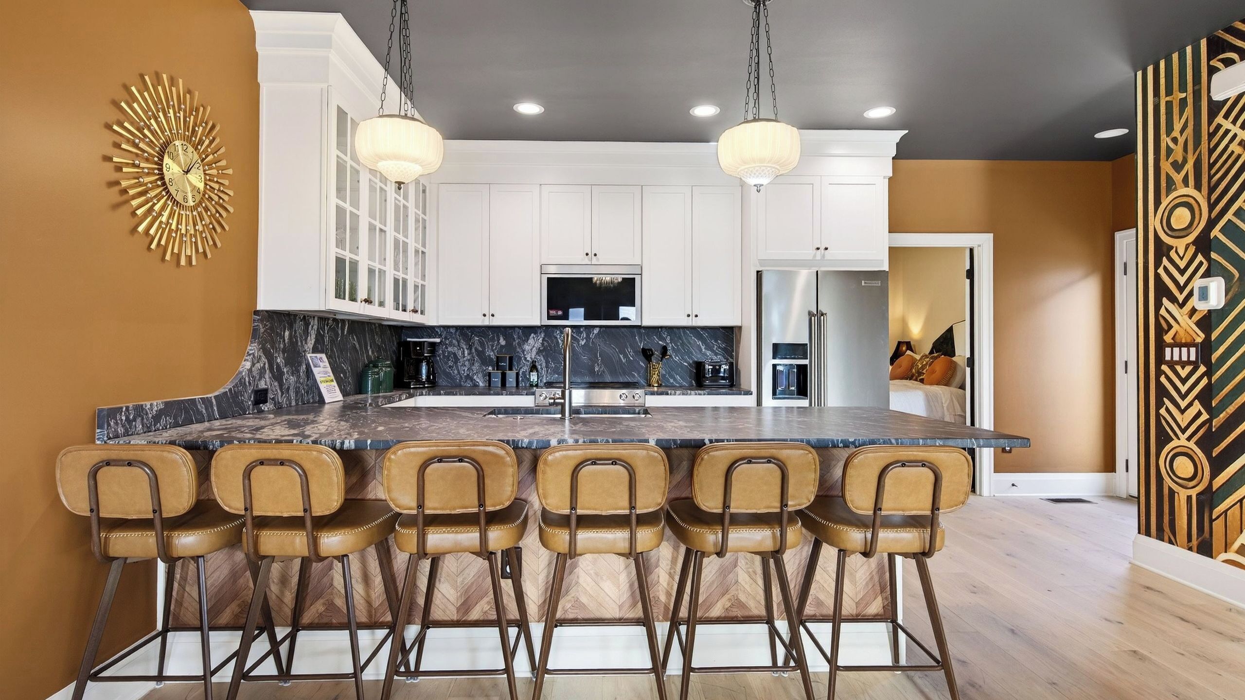 A modern kitchen with a central island, bar stools, and a decorative wall piece.