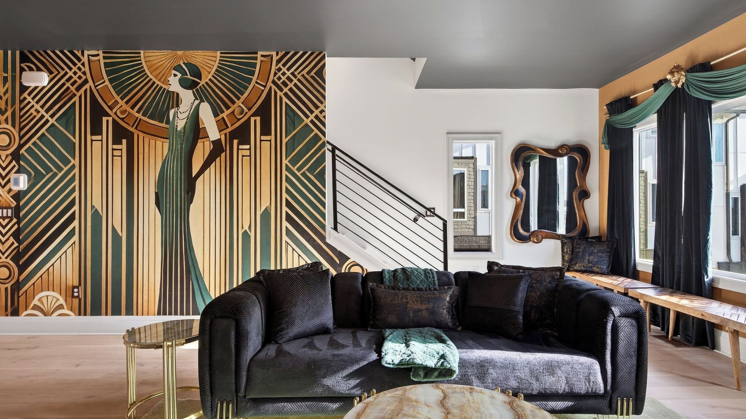 A modern living room with a geometric mural, a black sofa, and a staircase.