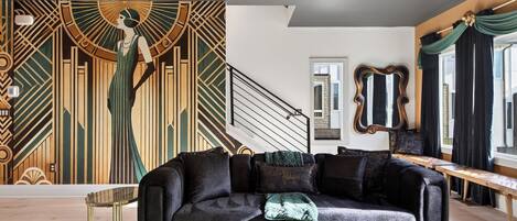 A modern living room with a geometric mural, a black sofa, and a staircase.