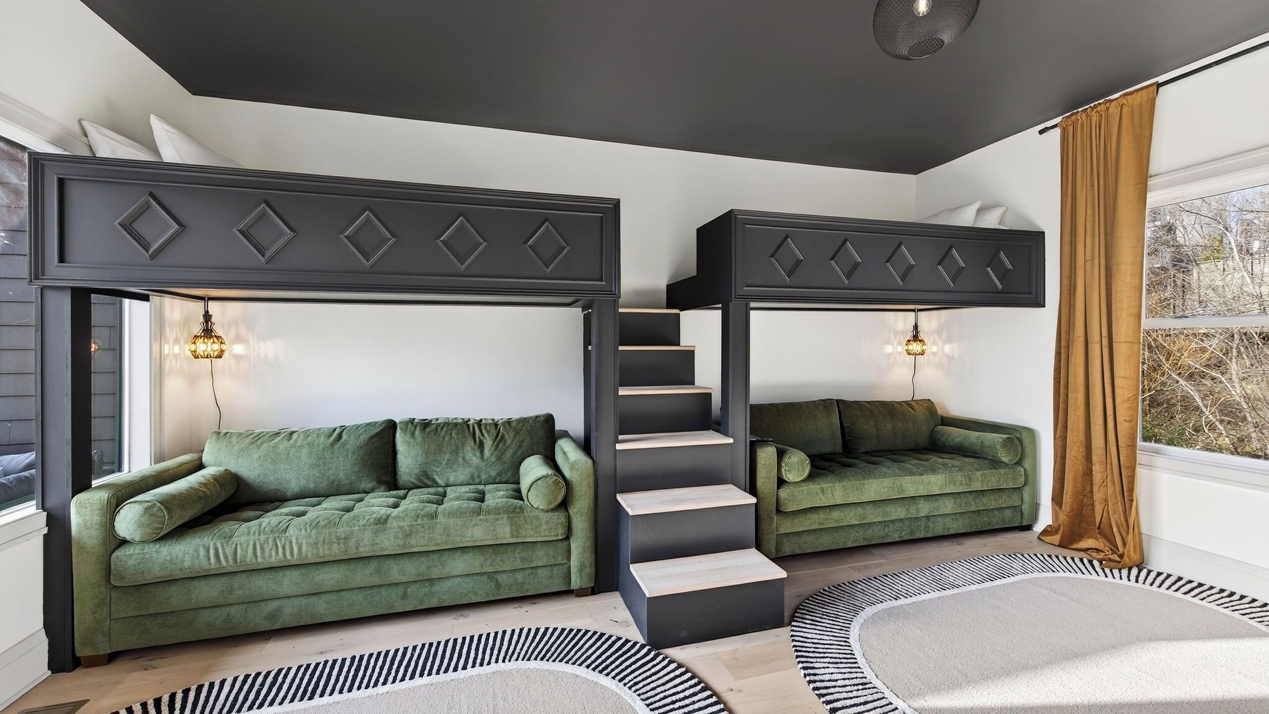 A room with two green sofas against a white wall, a black staircase, and a window with a view of trees.