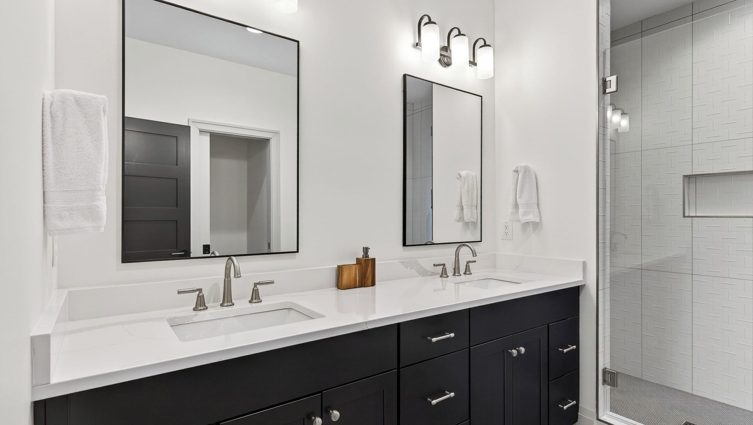 A modern bathroom with a white vanity, two sinks, a large mirror, and a shower area.
