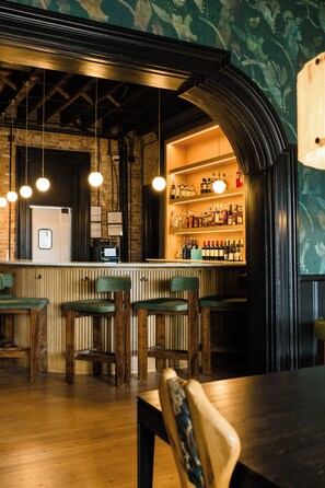 A bar area with wooden chairs, a counter with bottles, and a brick wall.