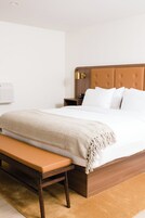 A neatly made bed with a wooden headboard, a bench at the foot of the bed, and a bedside table with a lamp.