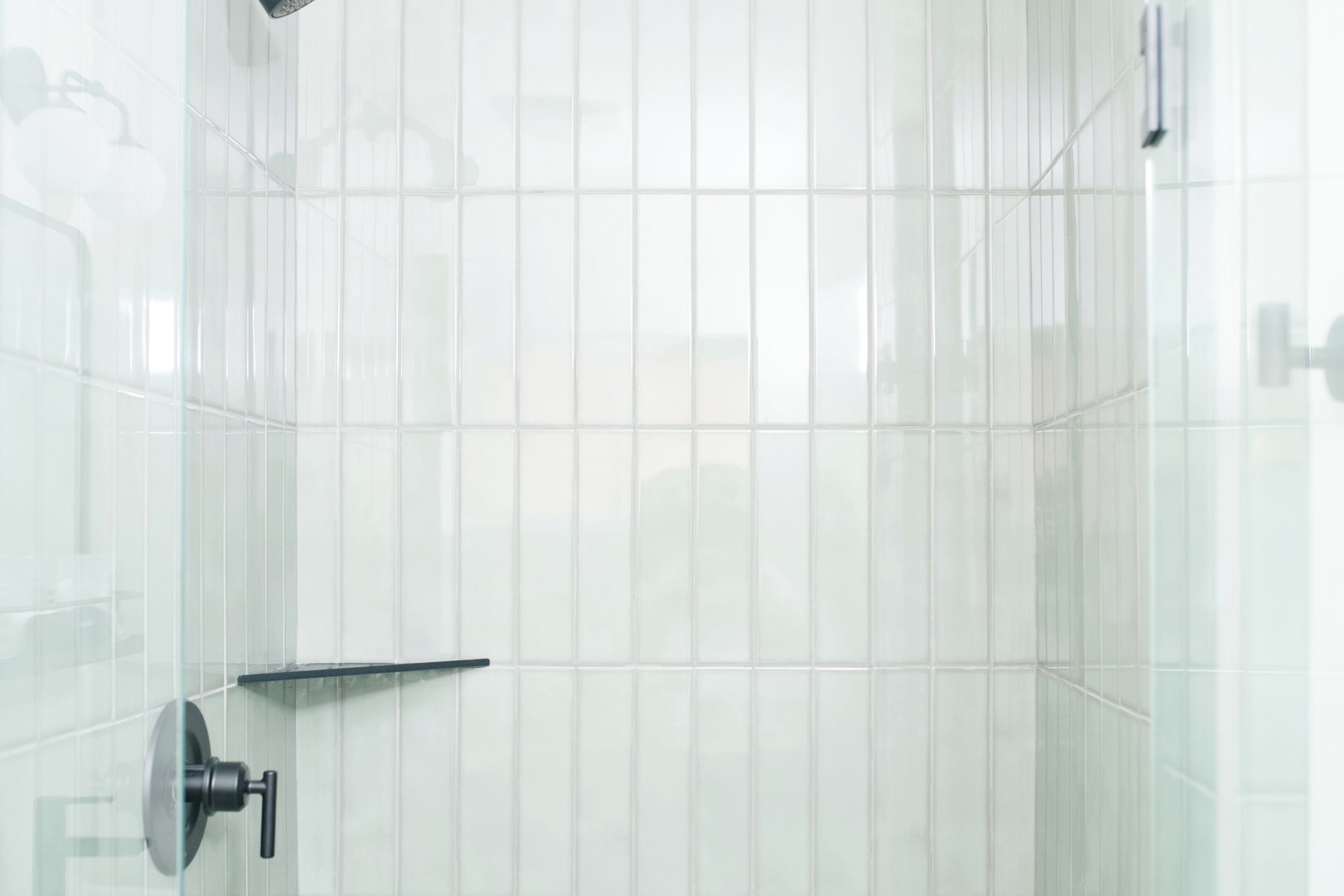 A bathroom with white tiled walls, a glass shower enclosure, and a black faucet.