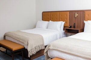 Una habitación de hotel con dos camas, un banco y una mesita de noche con un control remoto.