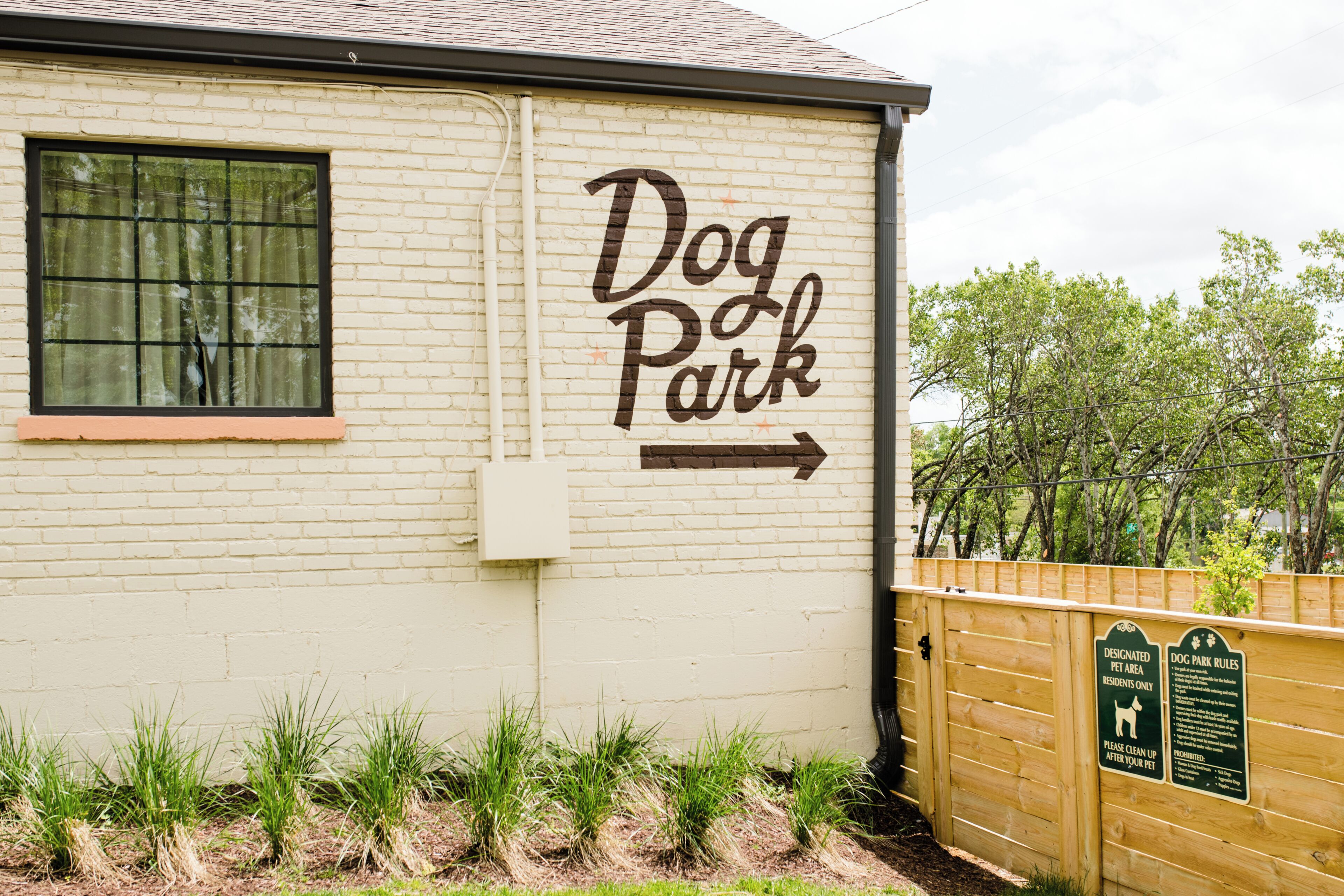 A building labeled 'Dog Park' with a directional arrow, a wooden fence, and a sign detailing park rules.