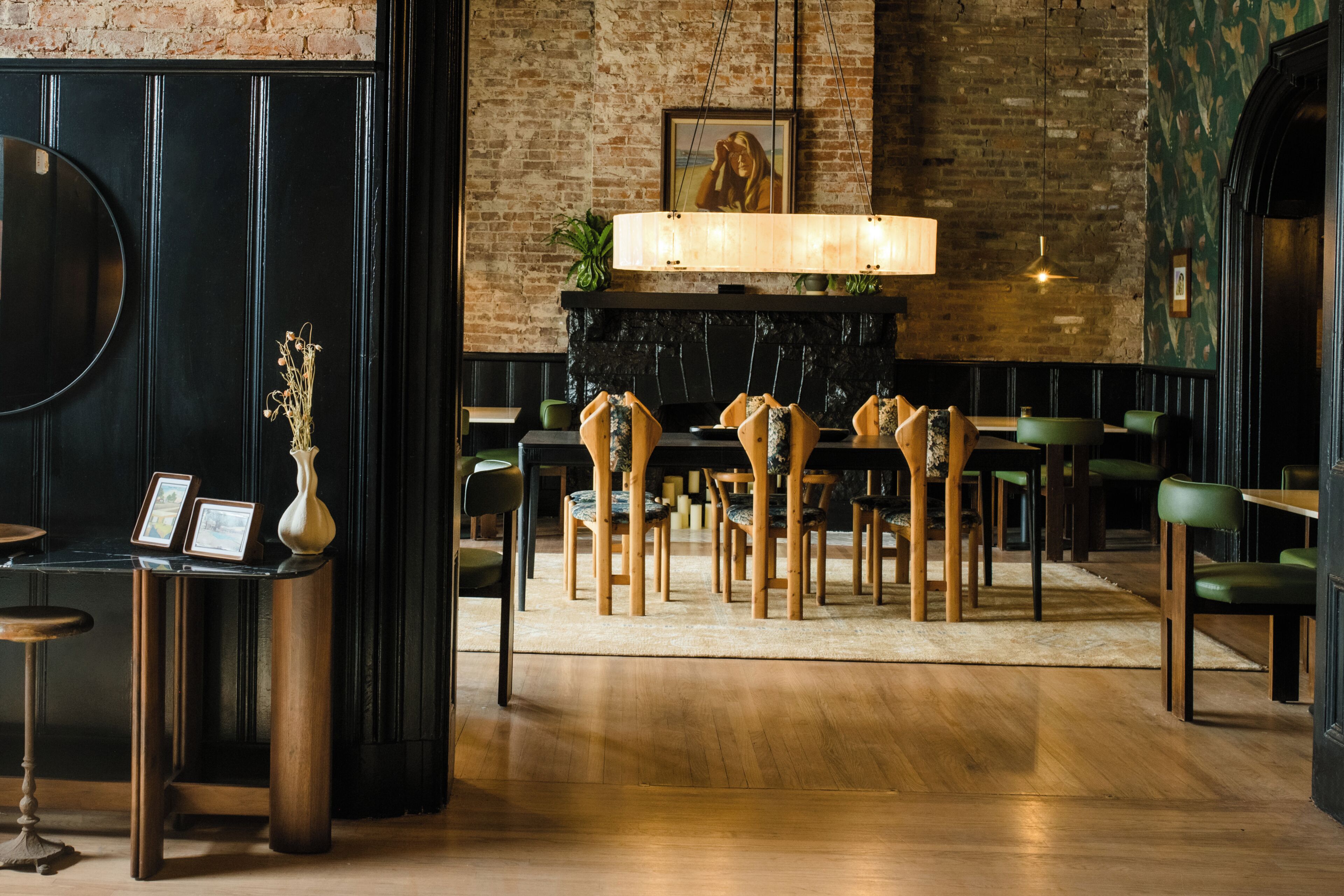 A restaurant with wooden chairs, a black wall, and a fireplace.