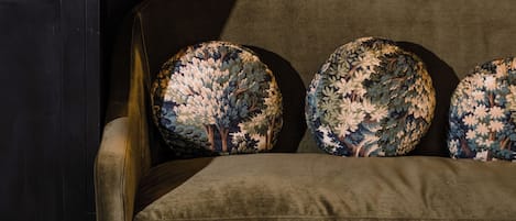 A green sofa with floral-patterned cushions, a dark-colored cabinet with books, and a painting on the wall.