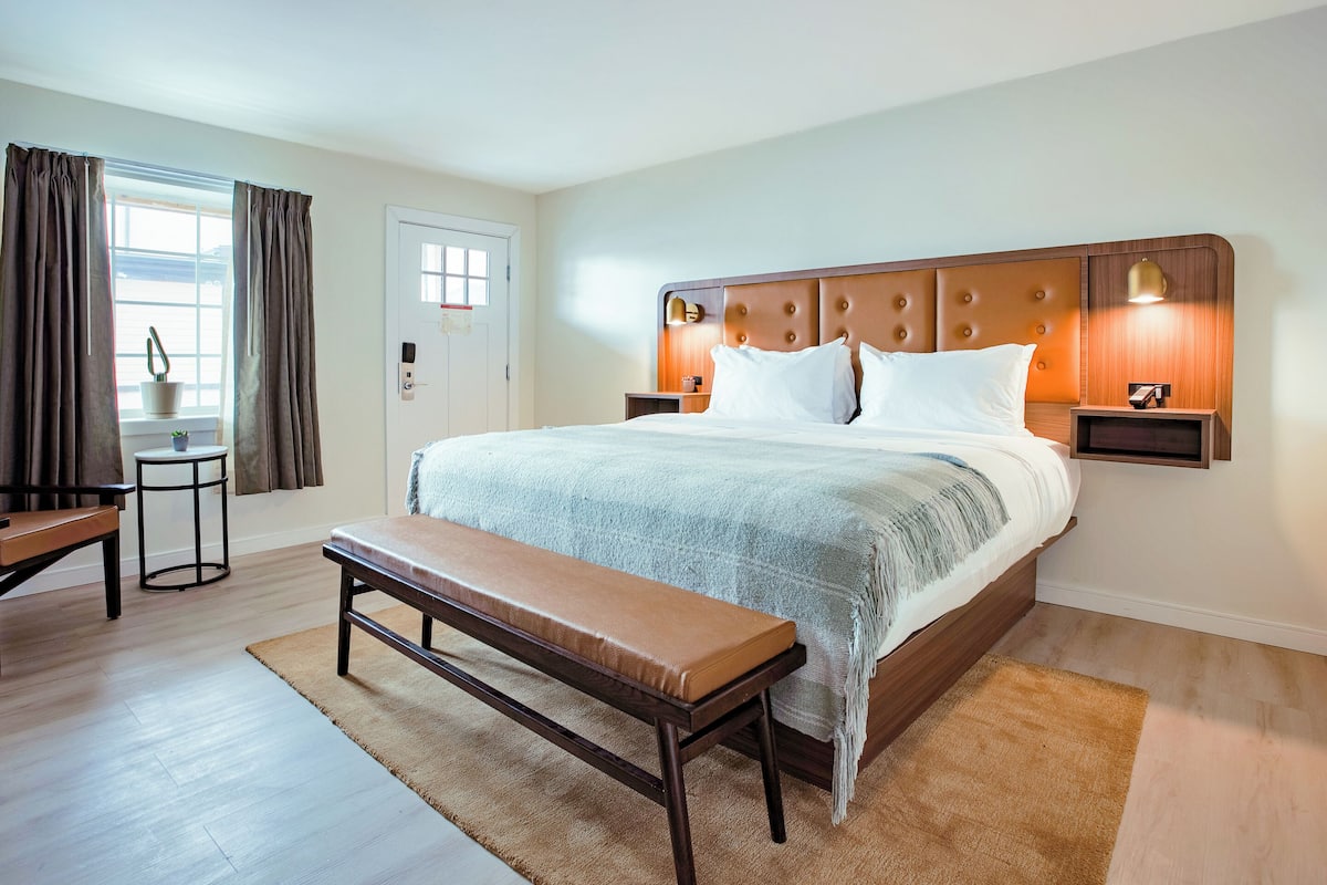 A neatly arranged bedroom with a bed, bedside tables, a bench, and a small table with a potted plant.